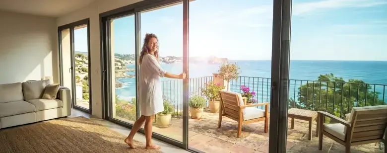Žena otevírá skluzavky vedoucí na balkon s výhledem do moře.