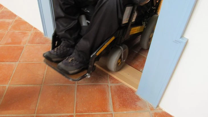 Křeslo v kolech projíždí dřevěným schodištěm přes prah dveří.