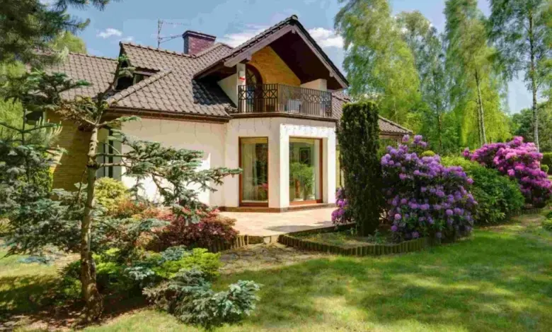Dům obklopený zahradou s vysokými stromy a keři v blízkosti zdi.