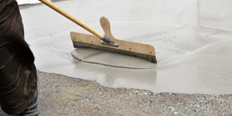 Pracovník vyrovnává čerstvý beton v garáži pomocí pravítka.
