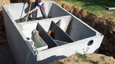 Muž instaluje betonový septik do vykopaného jámy.