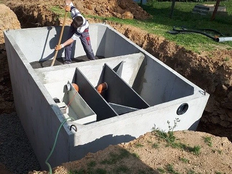 Muž instaluje betonový septik do vykopaného jámy.