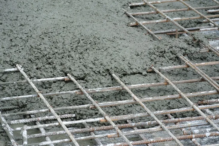 Mokrý beton přelévá se přes ocelovou výztuž na podklad.