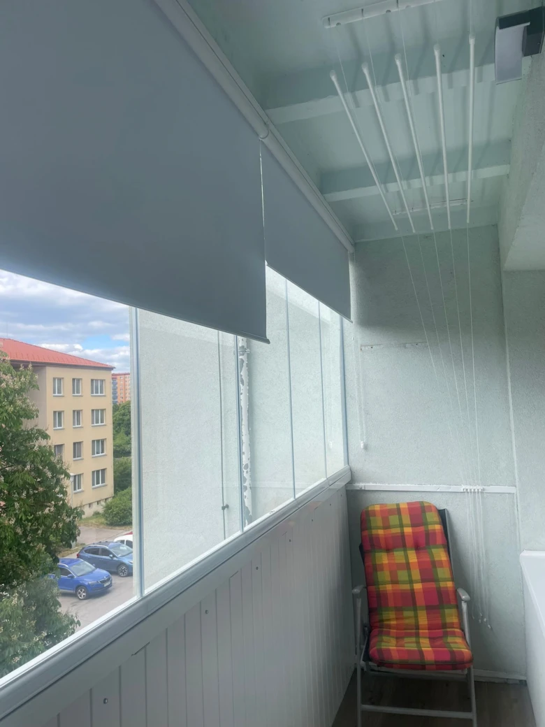 Balkon se zasklením sklem a roletami pro soukromí.