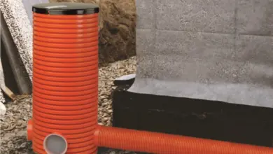 Oranžová drenážní trubice vedle základové stěny.