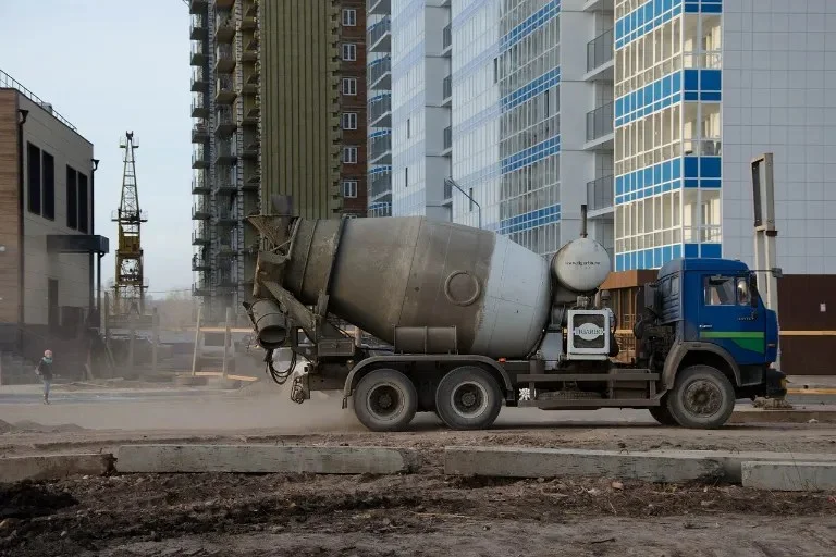 Modrý betonový smíchávač na staveništi s vysokými budovami.