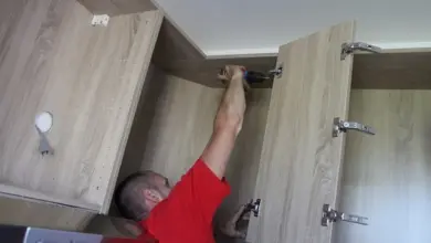 Muž upevňuje kuchyňskou skříň na stěnu pomocí vrtáku.