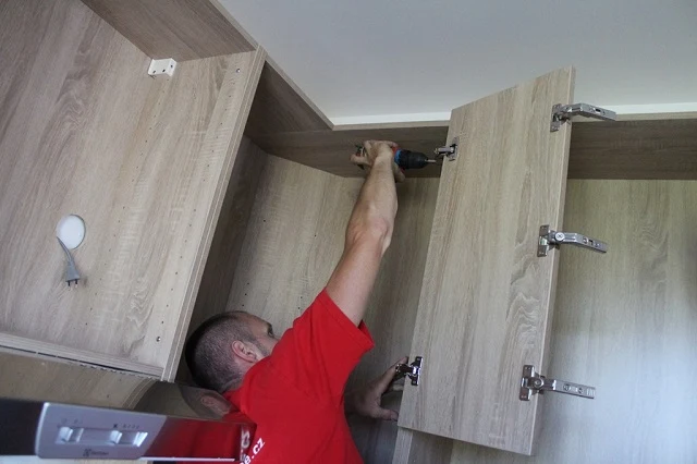 Muž upevňuje kuchyňskou skříň na stěnu pomocí vrtáku.