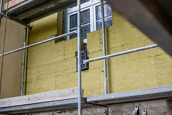 Žlutá nehořlavá minerální vlna na fasádě budovy pod šablonou.