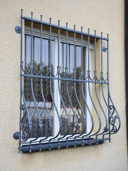 Černá železná mříž na okně s dekorativním designem.