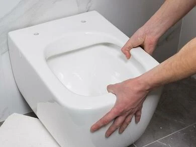 Muž instaluje bílou toaletu do zdi svépomocí.