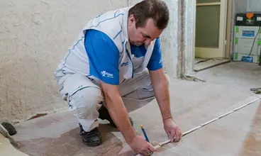 Muž měří podlahu pro instalaci sádrokartonu v koupelně.