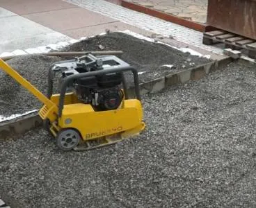 Žlutý vibrační tlumič vedle nově položených obrubníků na štěrku.