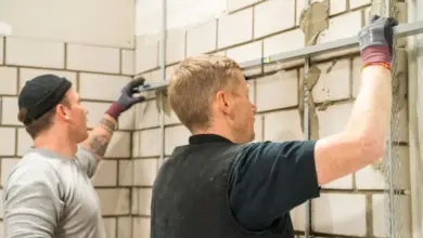 Dva dělníci montují síťovinu na vnitřní zdi před omítáním.