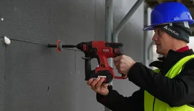 Stavebník vrtá do nosné zdi pro instalaci kotvy.