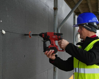 Stavebník vrtá do nosné zdi pro instalaci kotvy.