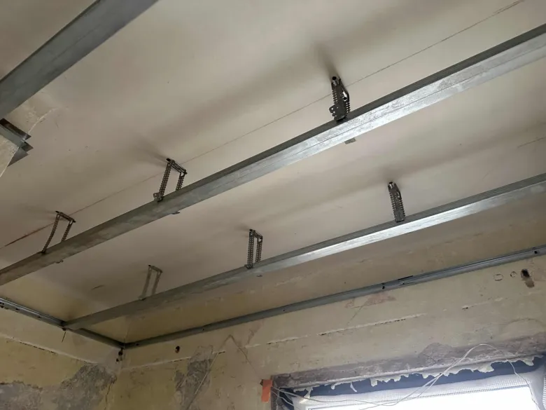 Krok instalace stropu s kovovými nosníky a závěsnými prvky.