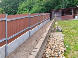 Dřevěný plot s betonovým základem na trávníku u letního sídla.