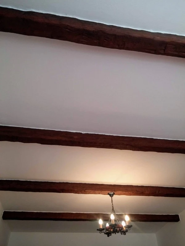 Falešné dřevěné trámy na bílém stropu s lustry.