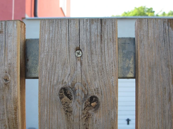 Detail dřevěného plotového prkna s šroubem a uzlem pro instalaci.