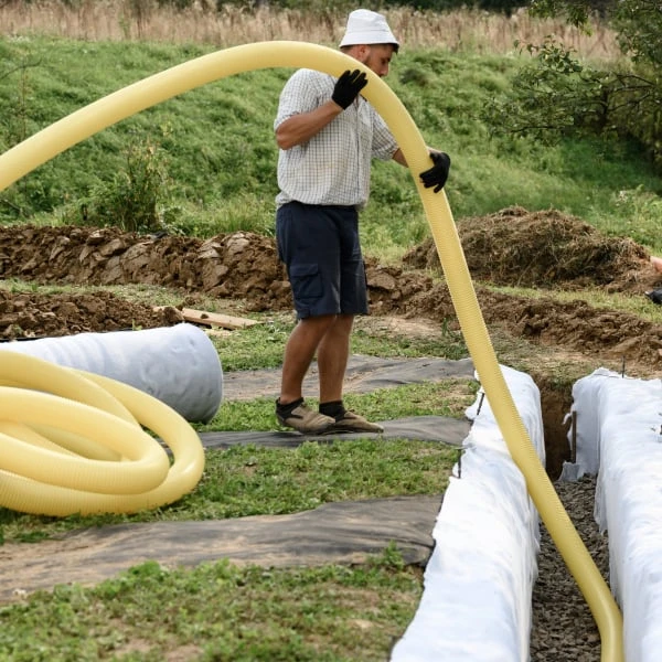Muž položí žlutou drenážní hadici do příkopu kolem domu.