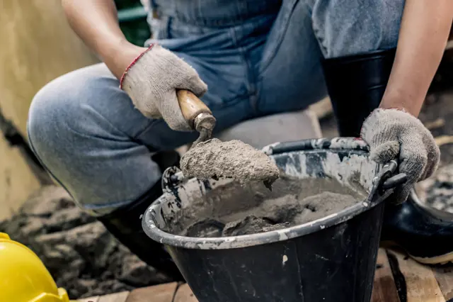 Stavebník míchá beton v kbelíku pomocí lopaty.