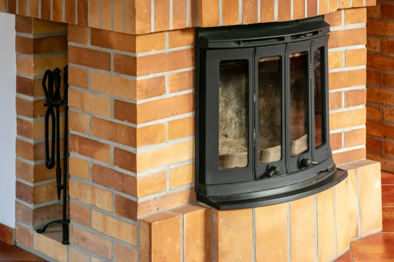 Černá dveře kamna v cihlovém krbu s nástroji vedle.