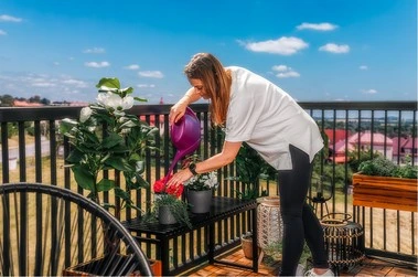 Žena zalévá rostliny na balkóně v bytovém domě.
