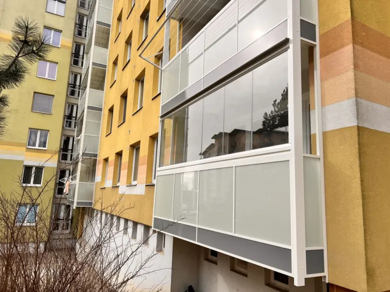 Moderní skleněné prodloužení balkonu na žlutém bytovém domě.