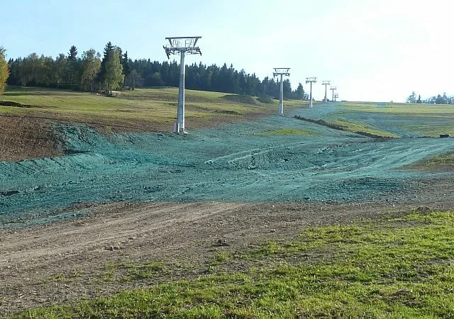 Zelená plocha s hydroosetem trávníku pod lanovkou.