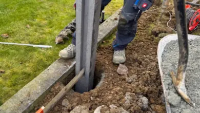Stavebník montuje sloup do betonu při stavbě plotu s nástroji na trávníku.
