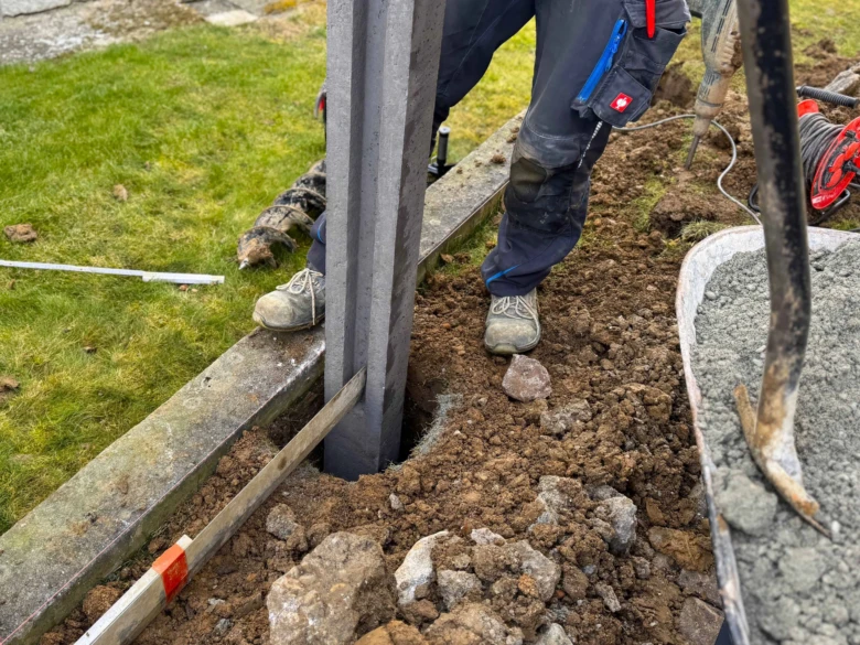 Stavebník montuje sloup do betonu při stavbě plotu s nástroji na trávníku.