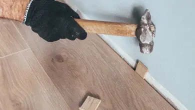 Ručník s kladivem zapichuje dřevěný kus do spáry mezi podlahou a zdí.
