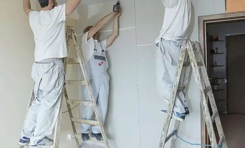 Tři muži montují stropní panely na kovové lišty.