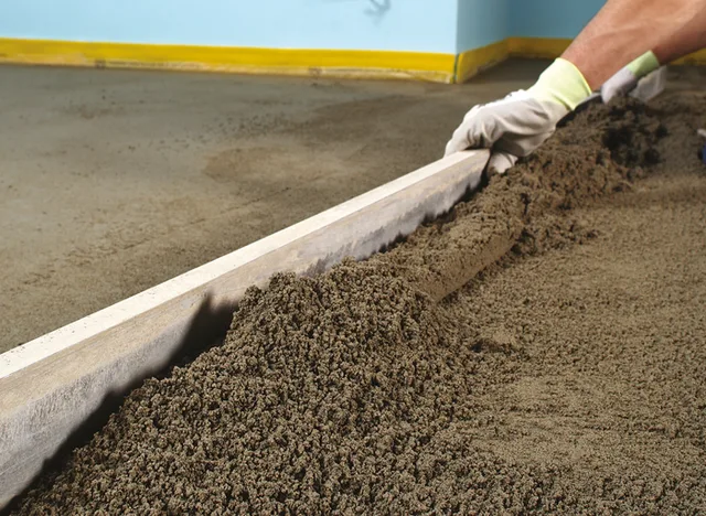 Pracovník vyrovnává vlhký samonivelační beton rovným hranolem.