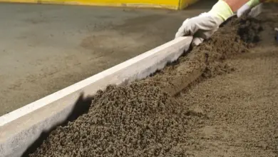 Ruce s rukavicemi vyrovnávají vlhký beton na podlaze.