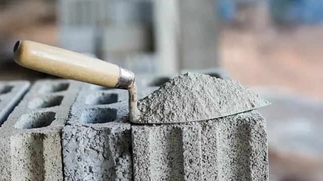 Kovová lopata s maltou na betonových cihlech.
