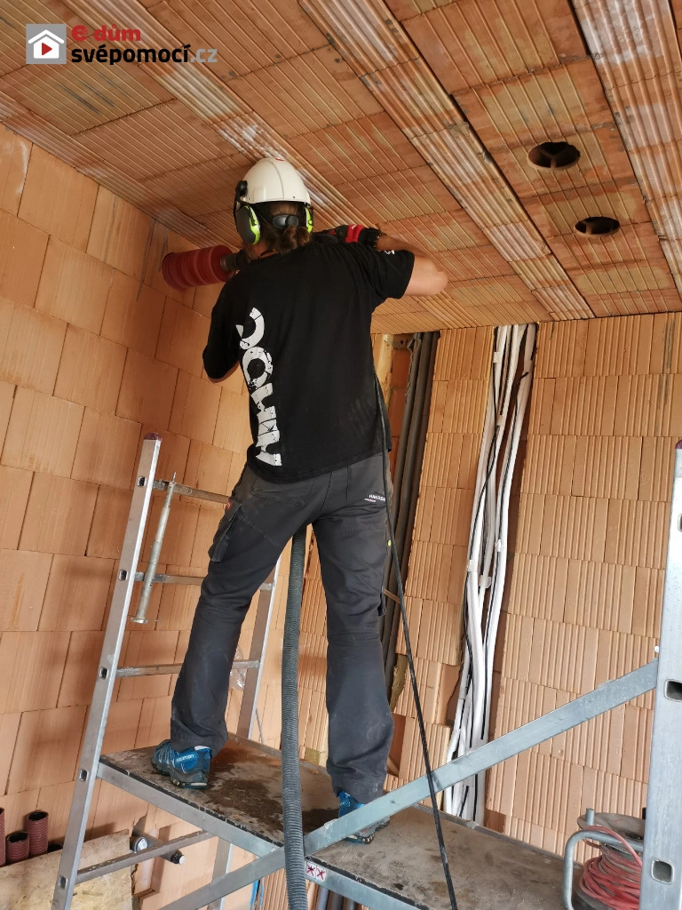Pracovník vyzbrojený bezpečnostním vybavením dělá otvor pro větrání ve stropě garáže.
