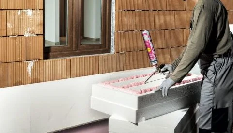 Stavebník nanáší roztavený polystyren na stěnu pomocí pistole.