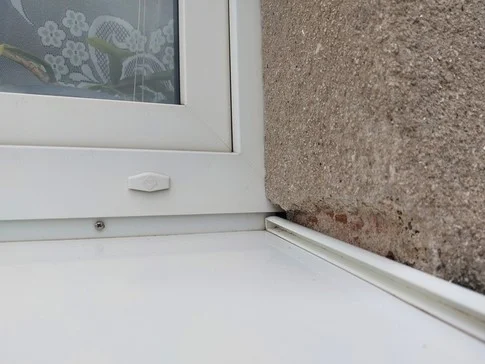 Detail bílého okenního parapetu se sklonem pro odvod vody.