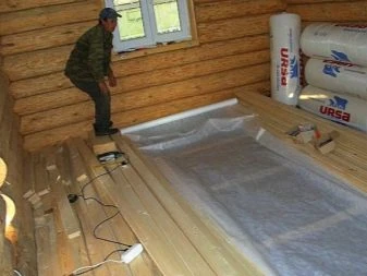 Muž instaluje parozábranu na podlahu v dřevěném domě s izolací.