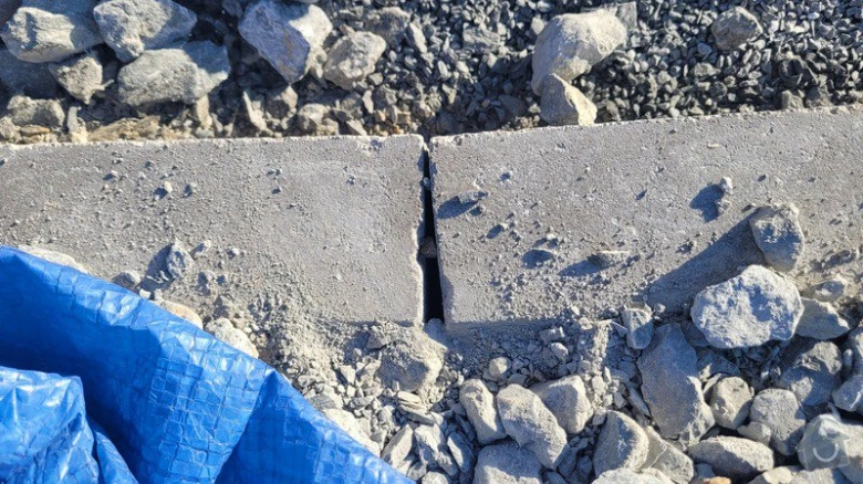 Poškozený betonový obrubník na zahradě s prasklinou mezi dvěma kusy.