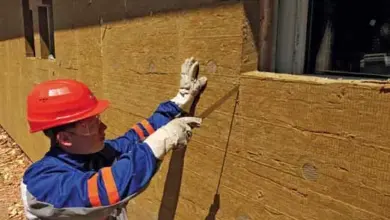 Stavebník montuje žlutou minerální vlnu na fasádu.