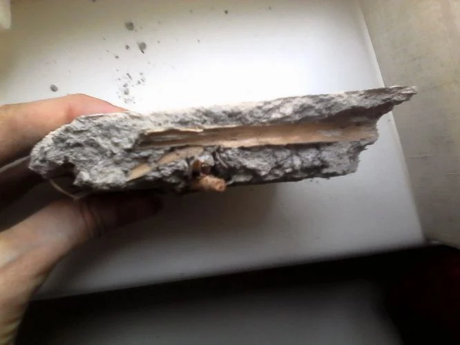 Rozbitá deska s odhalenou izolací poškozeného stropu.