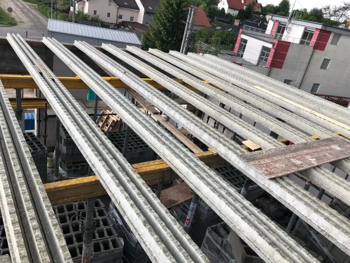Překližované betonové stropní trámy uložené na žlutých nosnících.