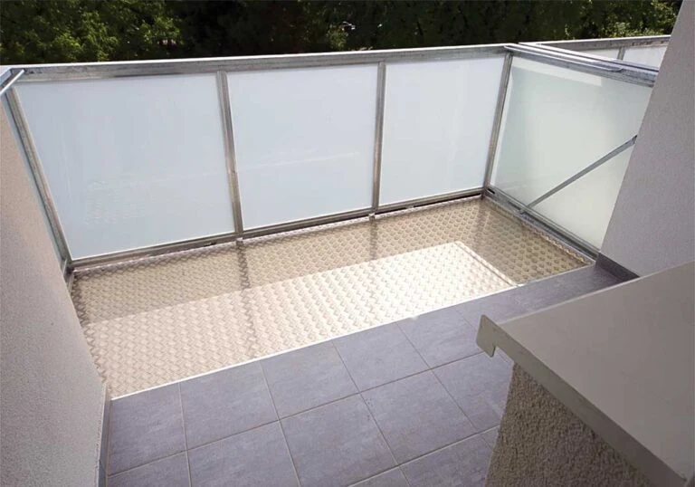 Nově vybudovaný balkon s průhledným skleněným zábradlím a texturovanou podlahovou deskou.