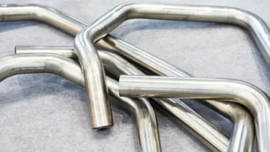 Náhodně uskladněné ohyby kruhových kovových trubek na šedé podložce.