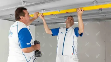 Dva muži montují sádrokartonový strop pomocí úrovně.