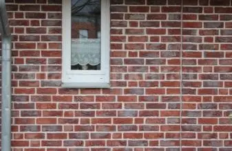 Červená cihlová zeď s bílým oknem pro výpočet počtu cihel.