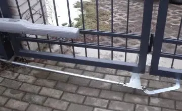Přerušený mechanismus sekčních vrat na dlažbě s hromadou sněhu v pozadí.